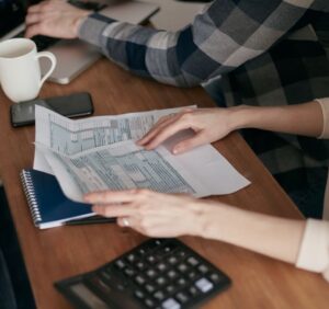 Hands organizing tax forms on a desk with a calculator and laptop
