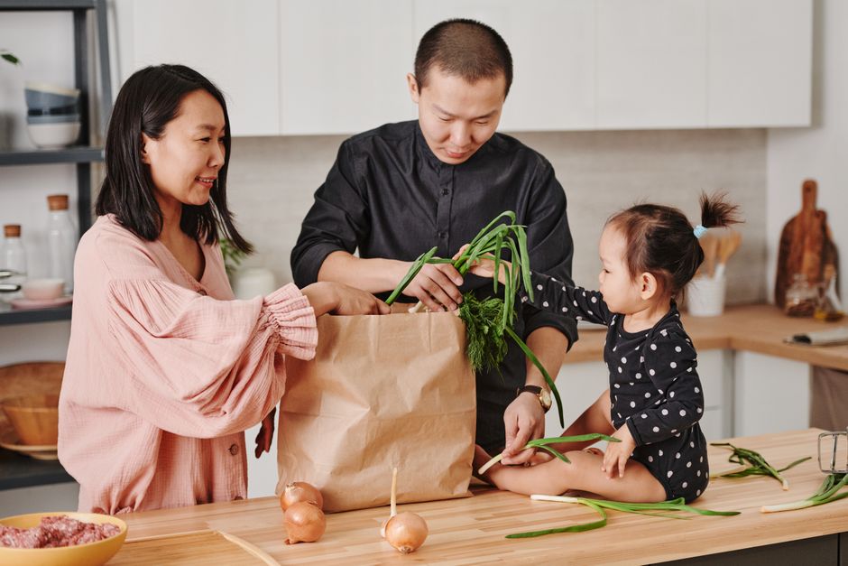 A family unpacking groceries together at a wooden kitchen table