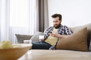 A man sitting on a sofa with a coffee, using his smartphone
