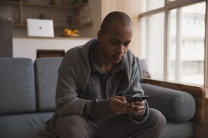A man sitting on a sofa at home reading a message on his smartphone