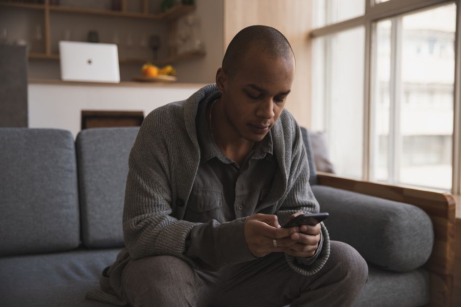 A man sitting on a sofa at home reading a message on his smartphone
