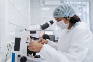 A researcher in protective gear analyzing samples with a microscope in a laboratory